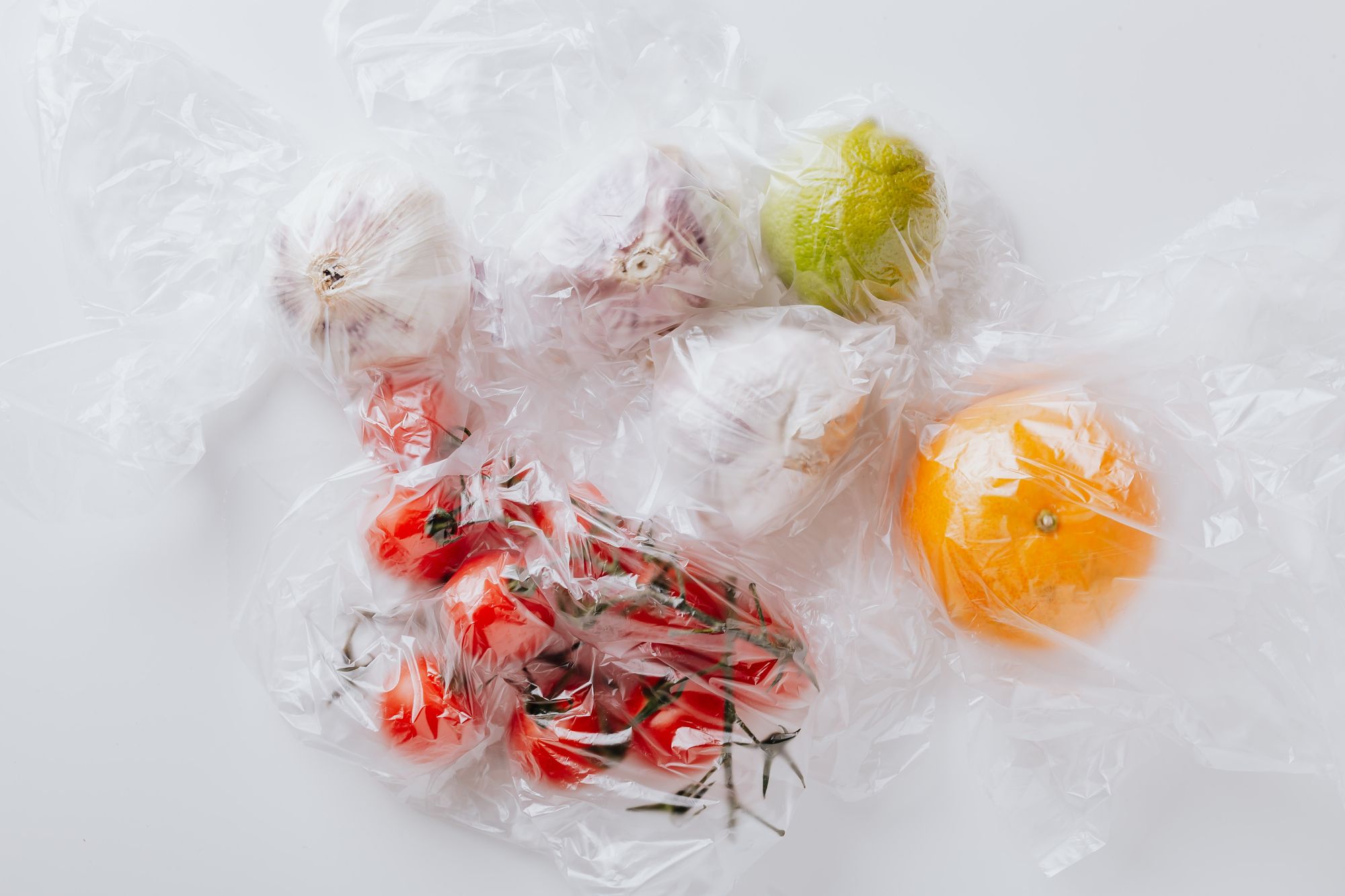 Garlic, tomatoes, lime, and an orange in plastic produce bags.