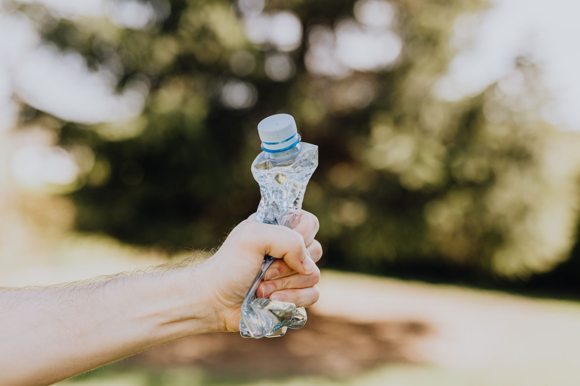 A hand crushing a plastic water bottle