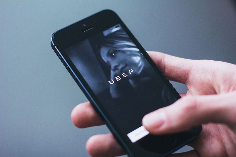 A hand holding an iPhone with their thumb presses a white button on the Uber page.