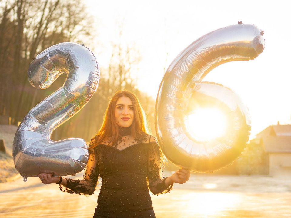 A woman holding balloons spelling "26"